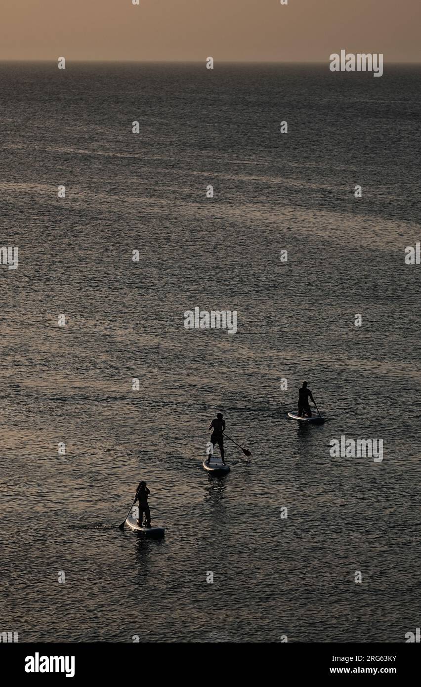 Silhouette di persone che pagaiano sul mare al tramonto. Foto Stock