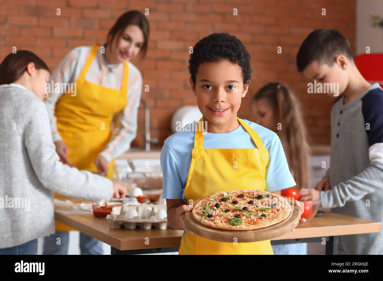 Piccolo ragazzo afro-americano con pizza preparata dopo la lezione di cucina in cucina Foto Stock