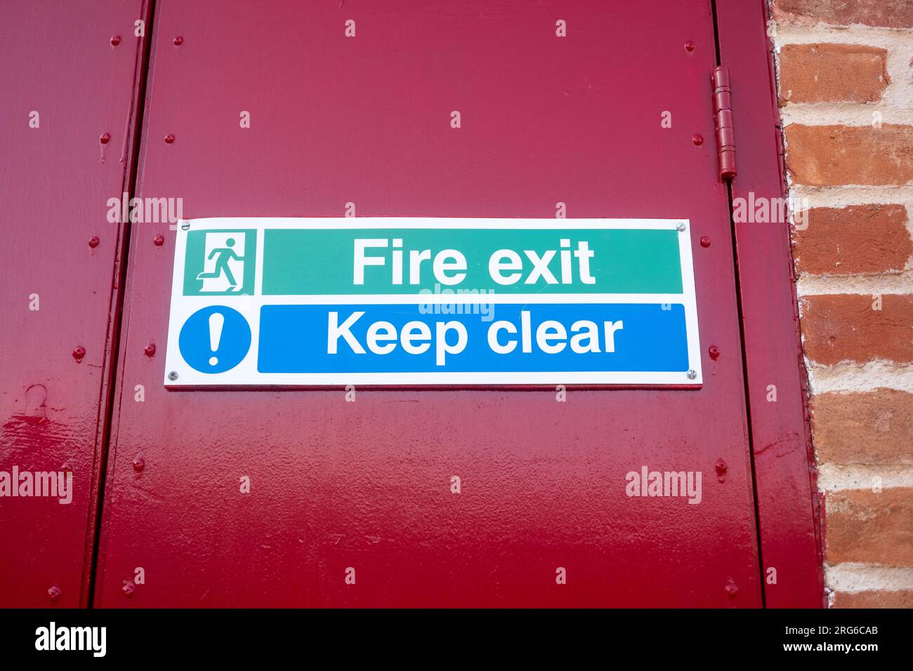 Uscita antincendio - tenere un cartello di sicurezza contro una porta rossa Foto Stock
