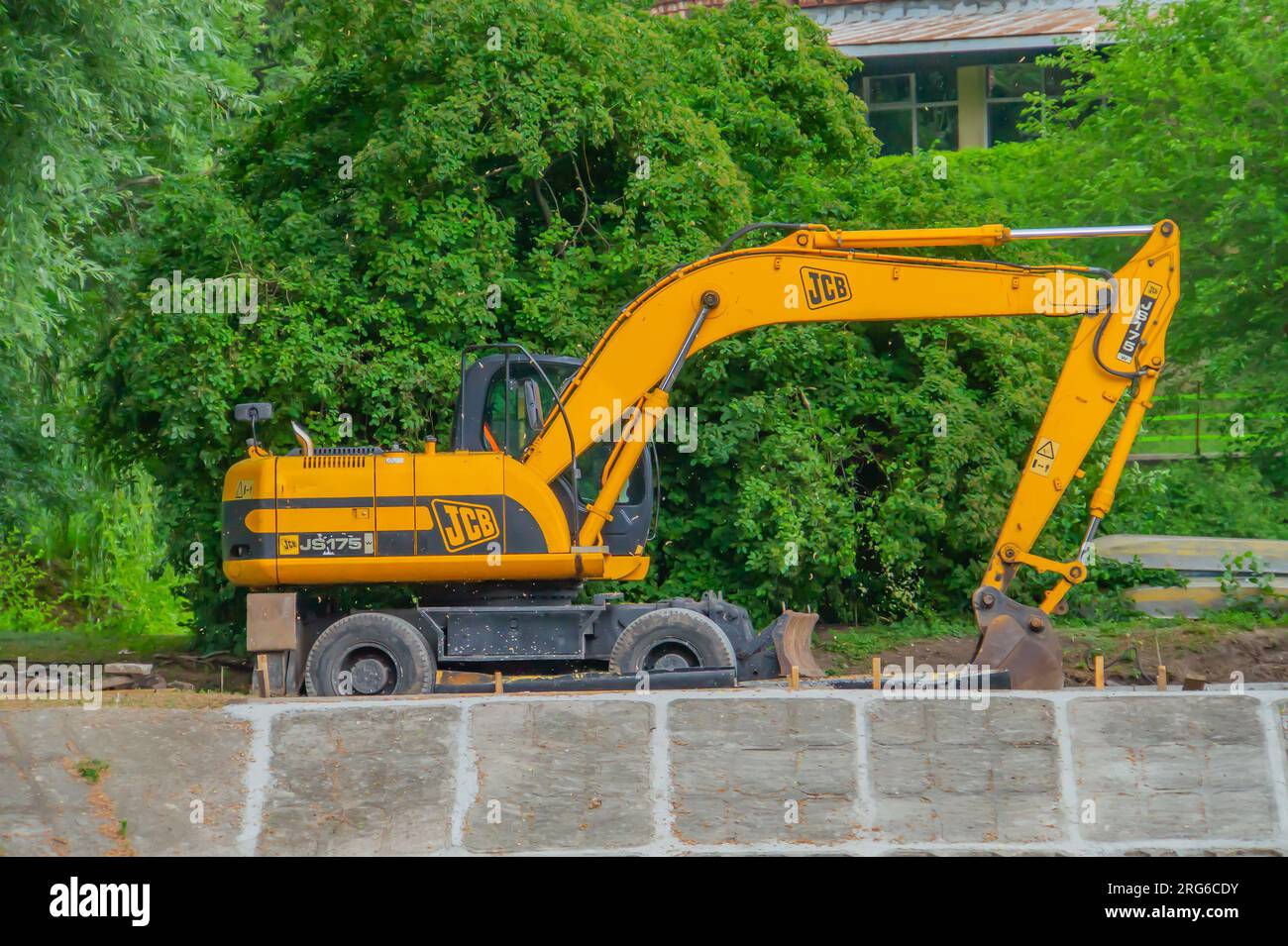 Vista frontale dell'escavatore cingolato per scavo in cantiere di demolizione in controluce. un escavatore sullo sfondo verde in un parco cittadino Foto Stock