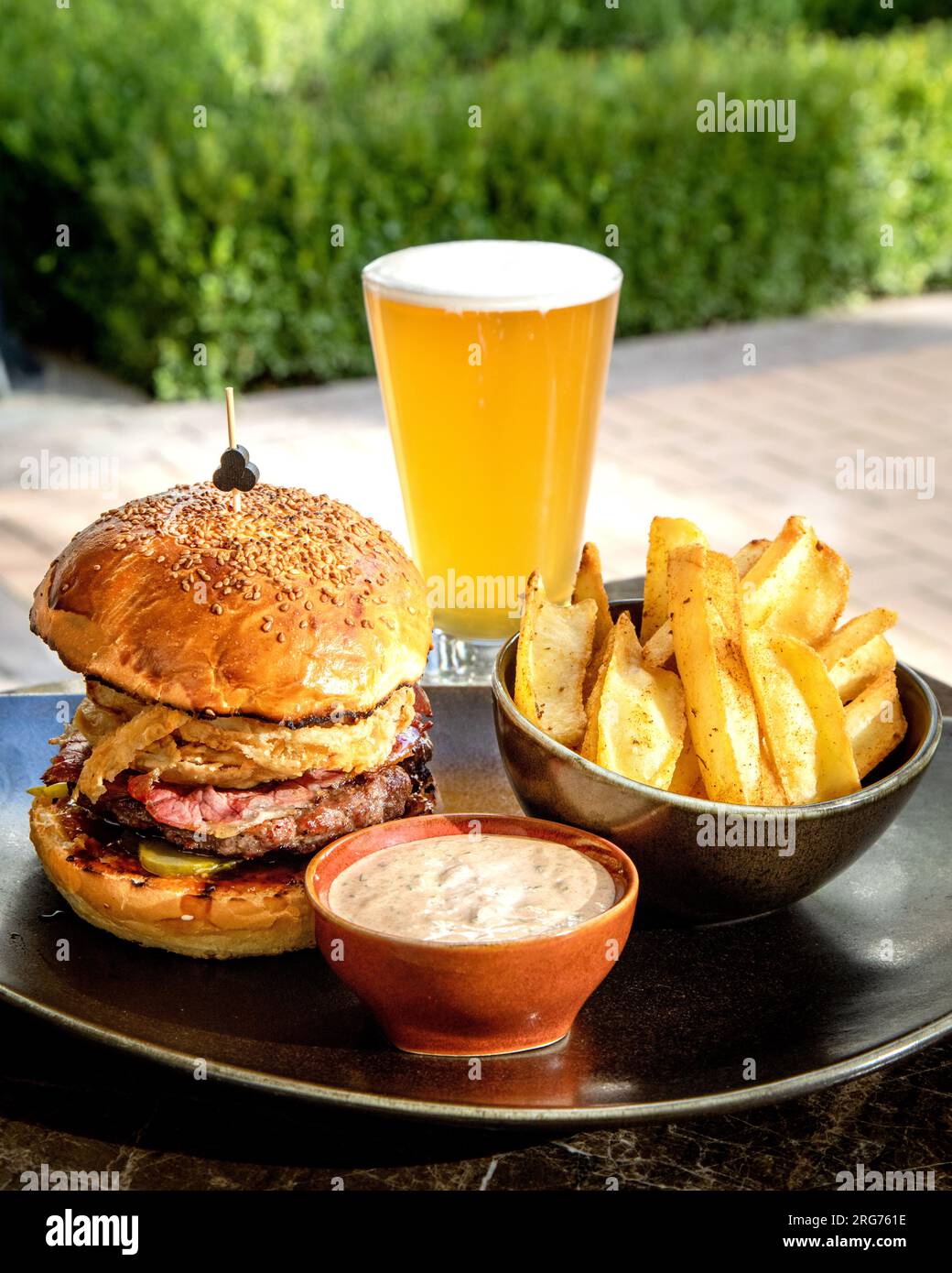 Gustosi cheeseburger con patate fritte in padella e un bicchiere di birra sul tavolo. Foto Stock