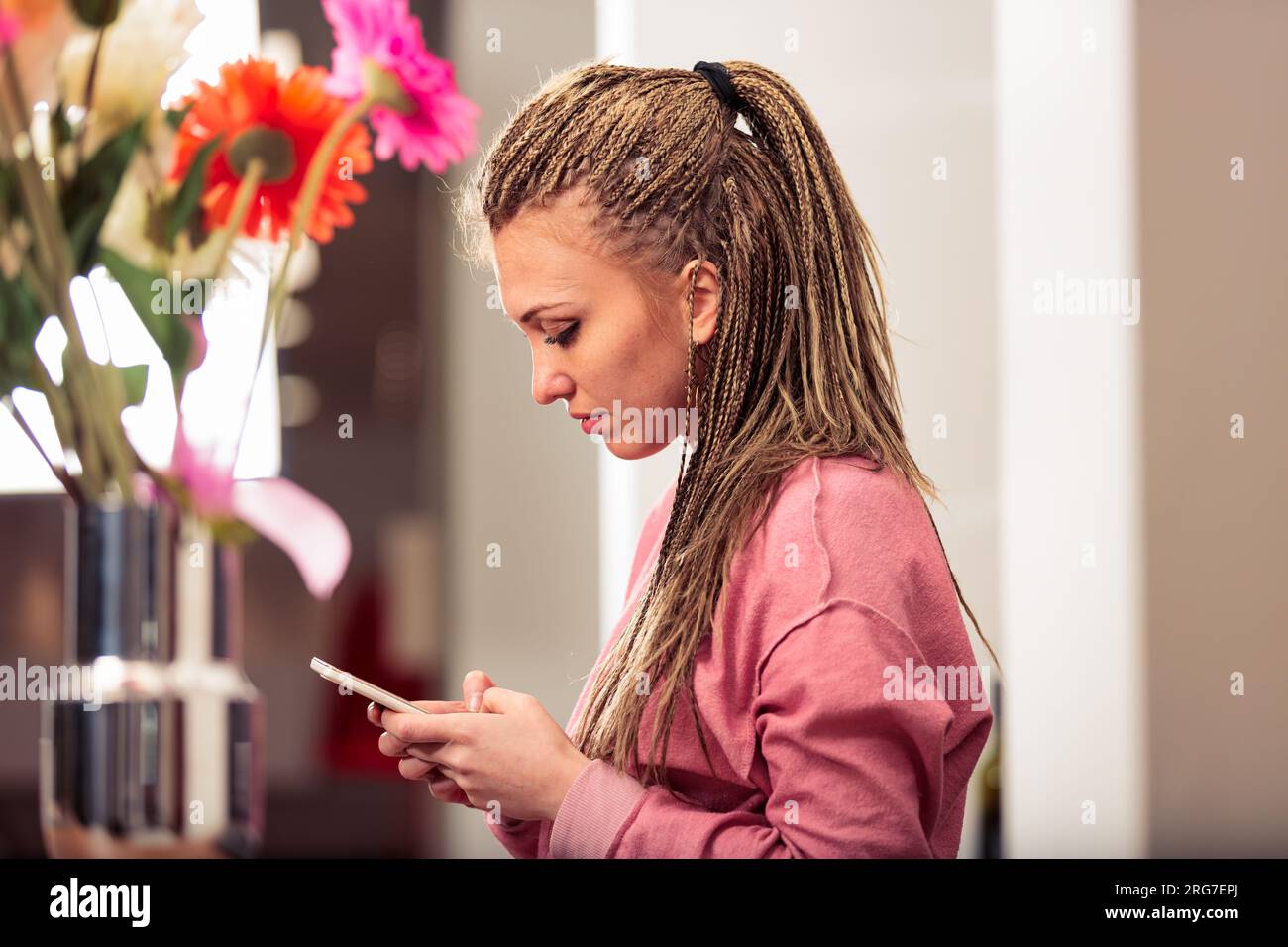 Nella sua cucina, una ragazza con trecce in una felpa rosa si impegna con giochi e app, intrattenimento moderno Foto Stock