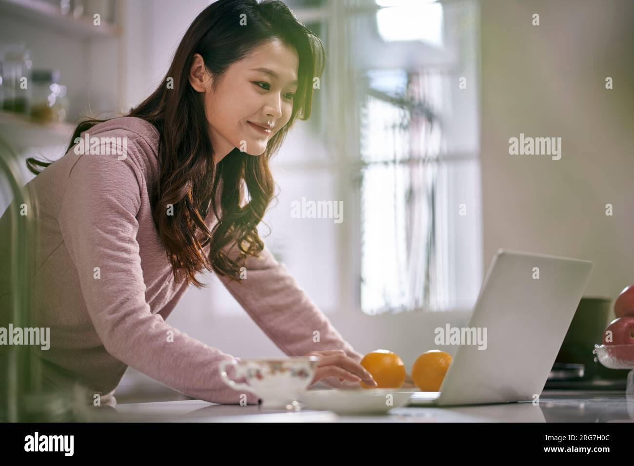giovane donna d'affari asiatica che lavora in cucina a casa utilizzando un computer portatile Foto Stock