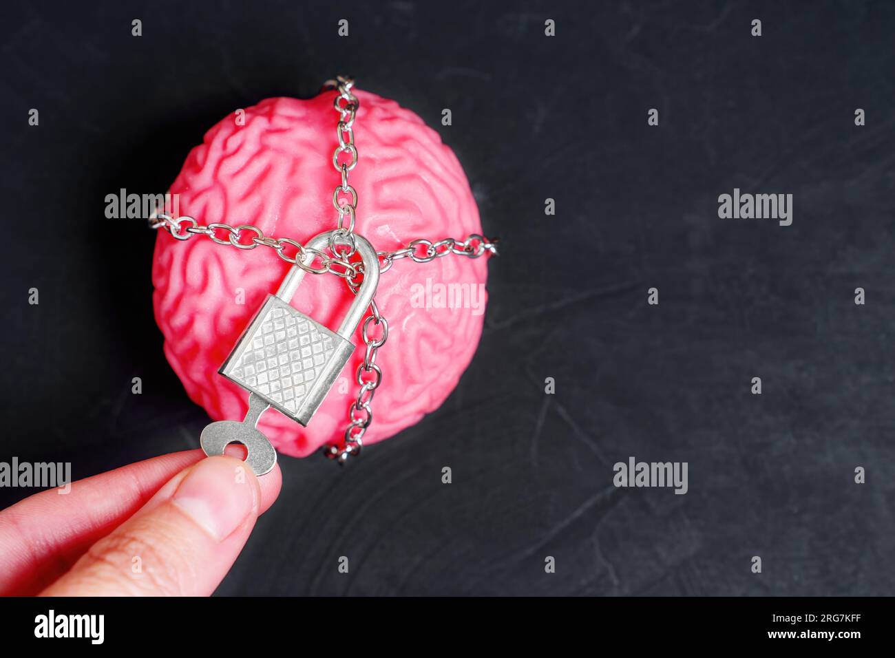 Cervello umano avvolto in catene e fissato con un lucchetto. La mano utilizza una chiave sul lucchetto. Foto Stock