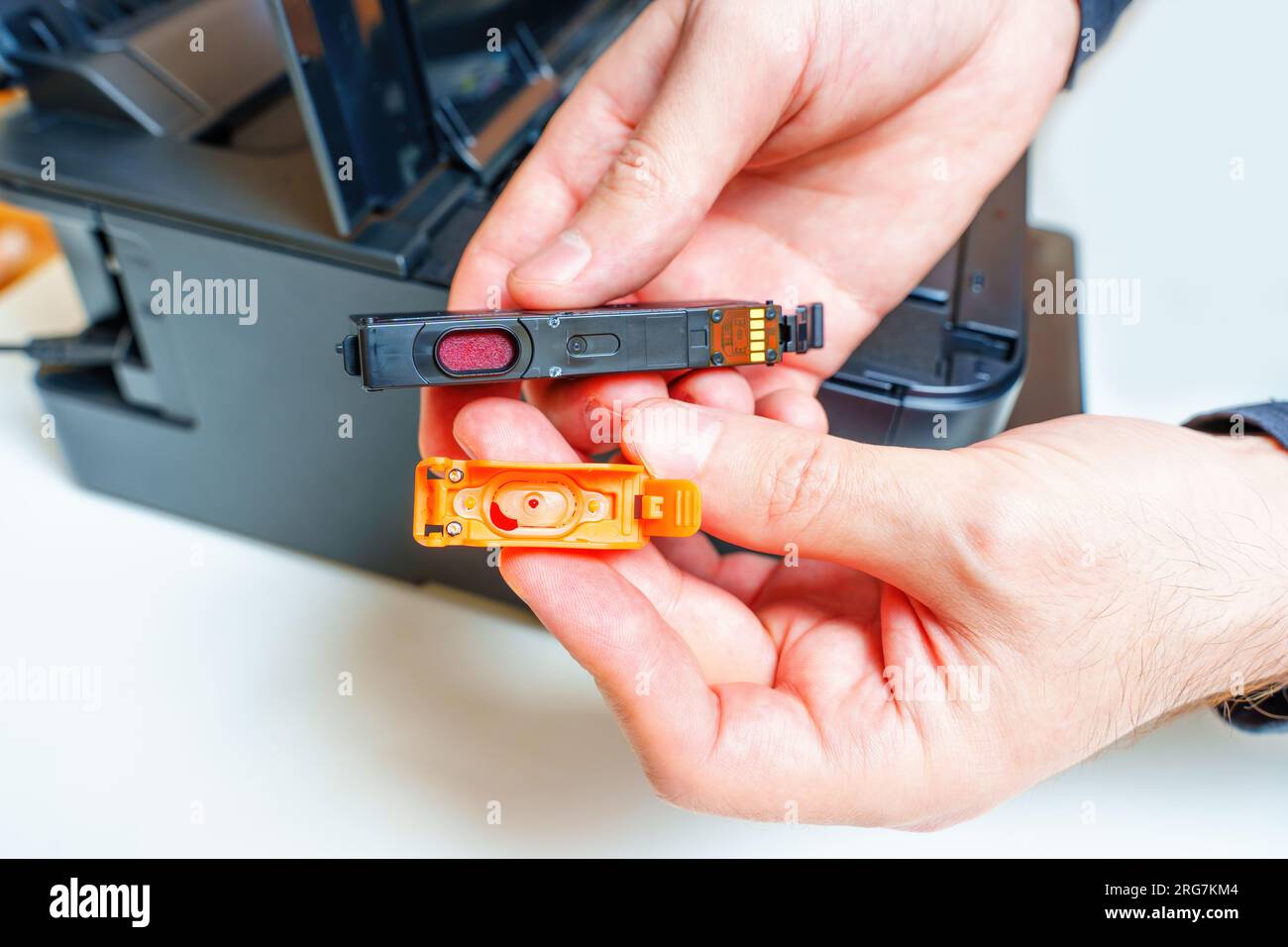 Vista ravvicinata della parte inferiore di un nuovo serbatoio d'inchiostro con il cappuccio di protezione rimosso subito prima dell'installazione nel set di stampanti a getto d'inchiostro nelle vicinanze. Foto Stock