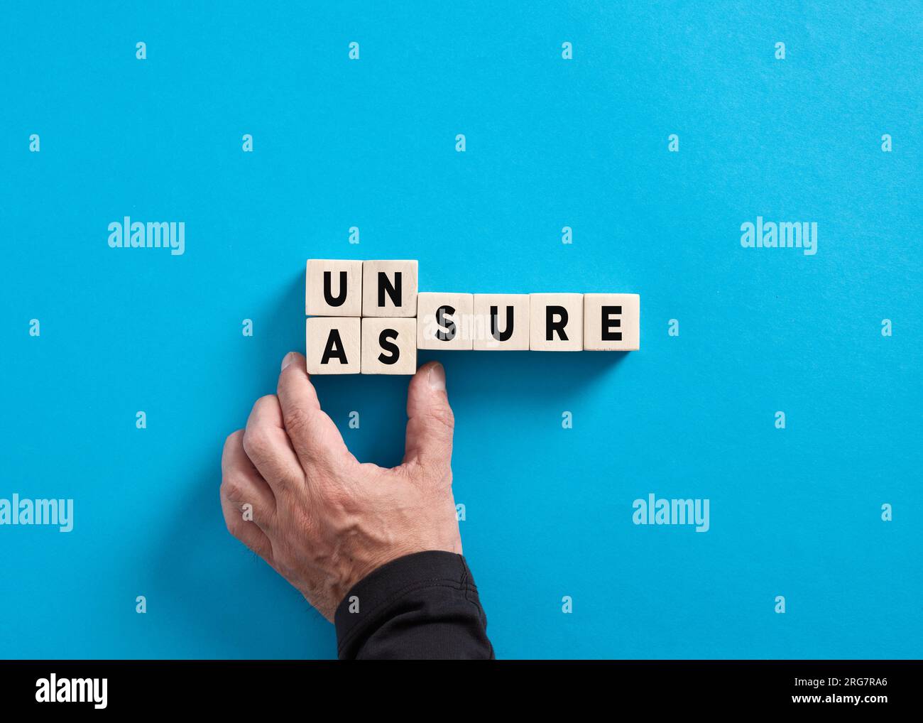 La mano maschile cambia la parola incerta per assicurare su sfondo blu. Concetto di garanzia aziendale, fiducia e fiducia. Foto Stock