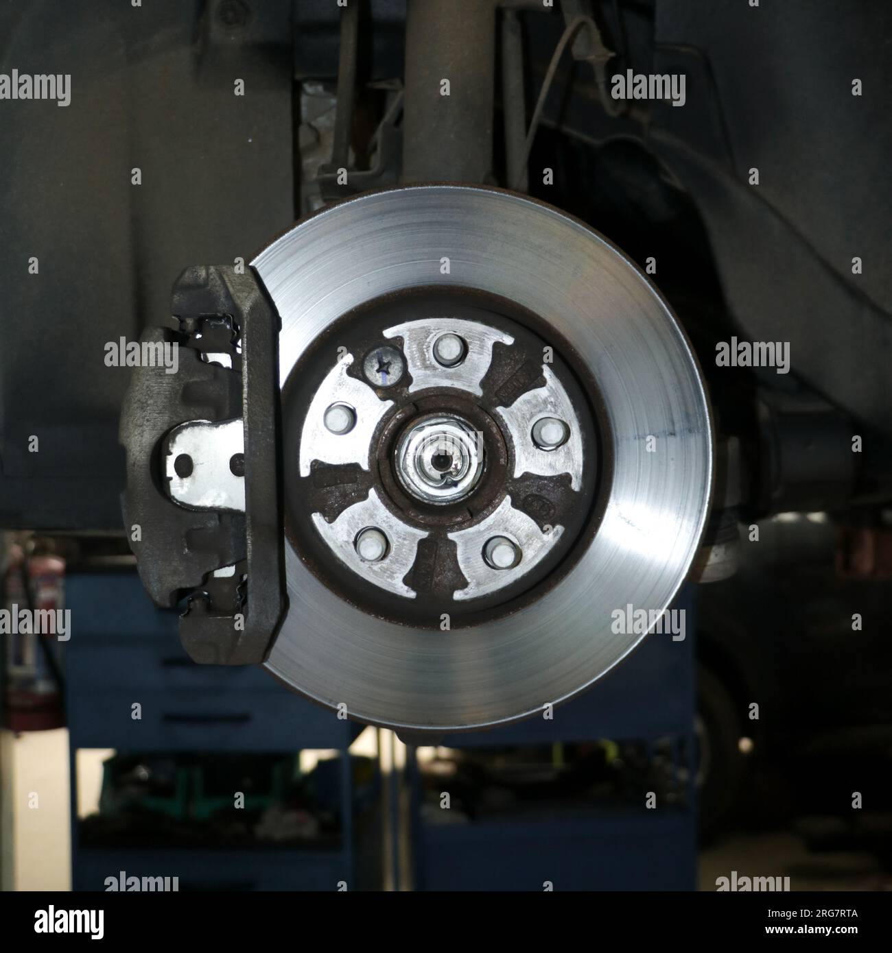 primo piano di un disco del rotore del freno per auto con pinza idraulica in manutenzione presso un centro di assistenza auto Foto Stock
