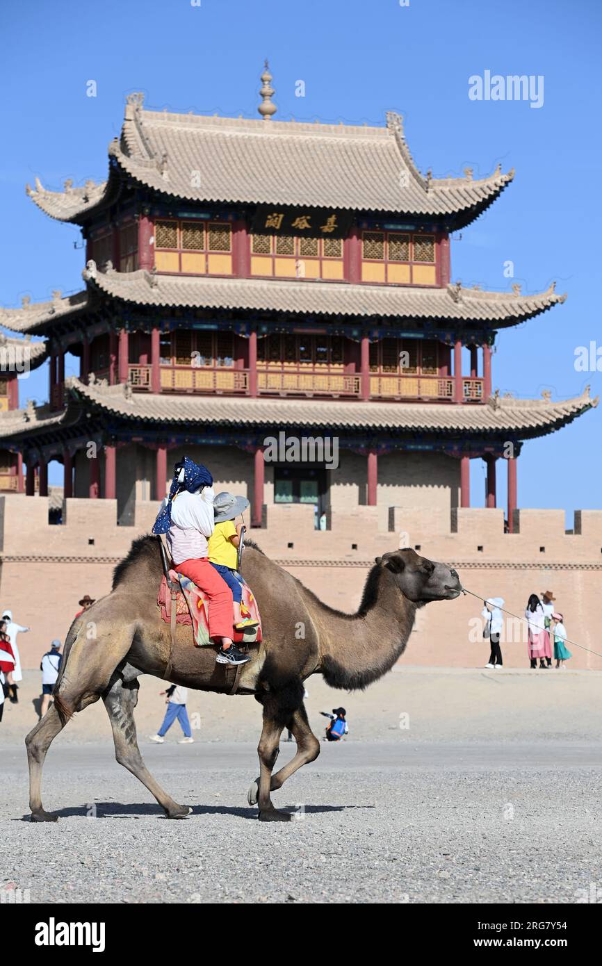 Jiayuguan, provincia cinese del Gansu. 7 agosto 2023. I turisti cavalcano su un cammello all'esterno del passo Jiayu nella città di Jiayuguan, provincia del Gansu della Cina nord-occidentale, 7 agosto 2023. Il passo Jiayu, una famosa parte della grande Muraglia costruita durante la Dinastia Ming (1368-1644), ha attirato un numero crescente di visitatori durante la stagione turistica estiva, con oltre 30.000 visitatori al giorno in picco. Crediti: Fan Peishen/Xinhua/Alamy Live News Foto Stock