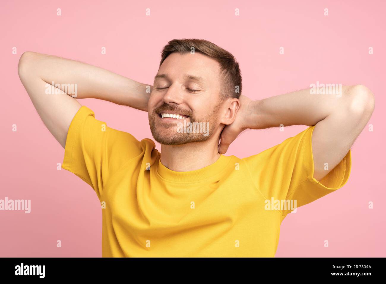 Uomo sorridente felice e soddisfatto con le mani dietro la testa che sogna, riposandosi sullo sfondo rosa dello studio Foto Stock