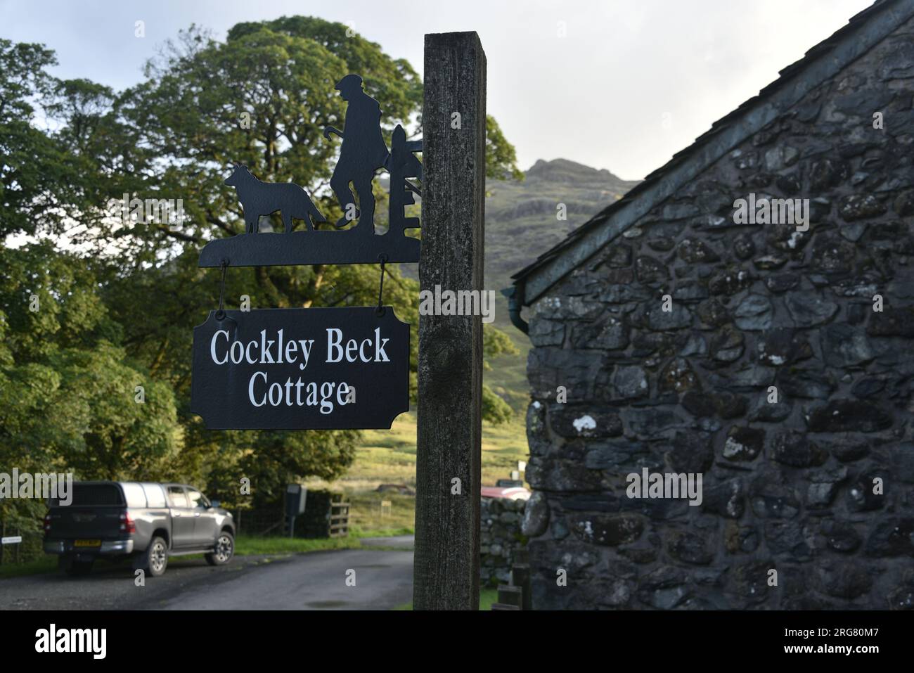 Cockley Beck, Duddon Valley, Lake District National Park, 8 agosto 2023. Il muro del cottage Cockley Beck (a destra) è attaccato alla Cockley Beck Farm; cartello per il cottage per informare la gente dove si trova; la luce dell'alba, a Cockley Beck, Lake District National Park, Cumbria, Regno Unito. Credito: Terry Waller/Alamy Live News Foto Stock