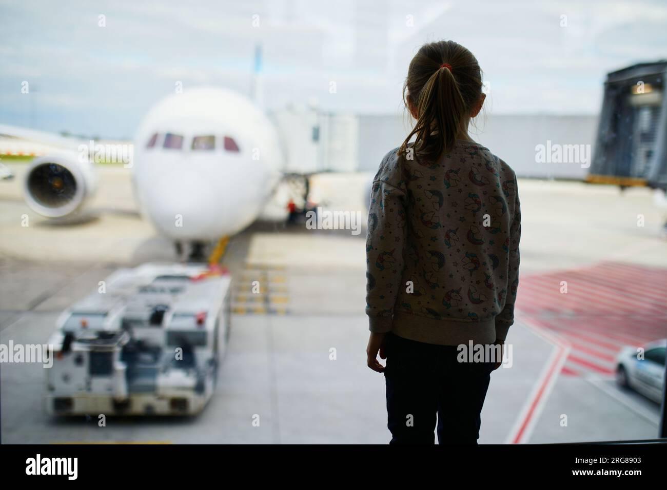 Silhouette di una bambina prescolare all'aeroporto internazionale, che guarda dalla finestra gli aerei. Viaggia con il concetto dei bambini Foto Stock