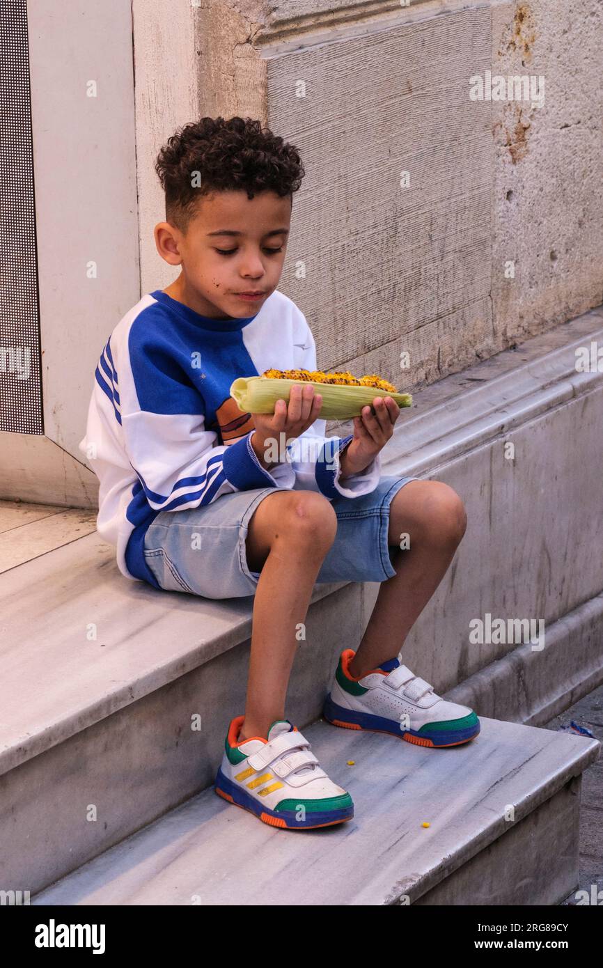 Istanbul, Turchia, Türkiye. Istiklal Street, Young Boy Eating Roasted Corn on the Cob. Foto Stock