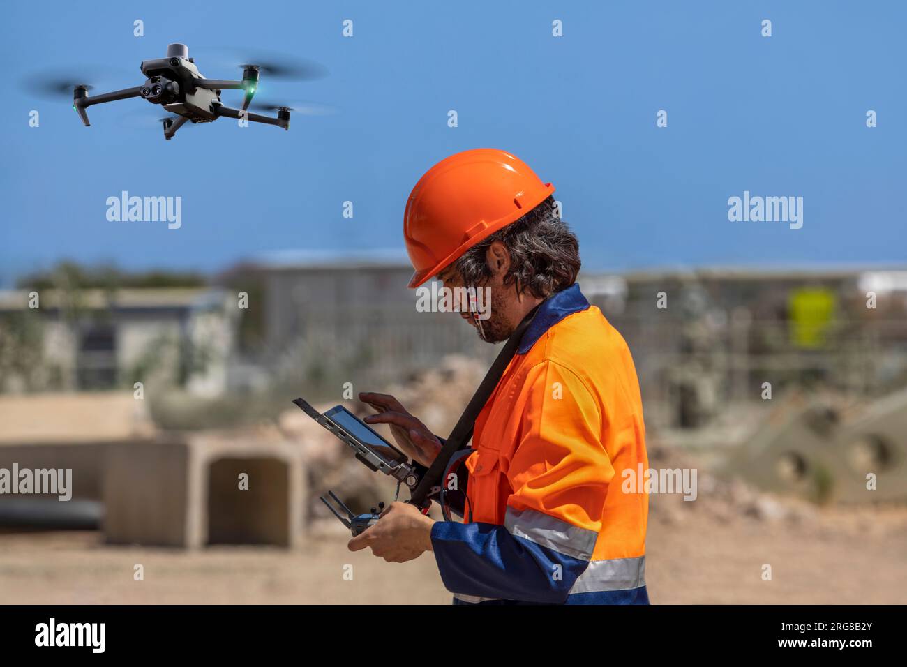 Operatore di droni con telecomando per una telecamera UAV termica, che esegue il rilevamento di un cantiere in un'area industriale Foto Stock