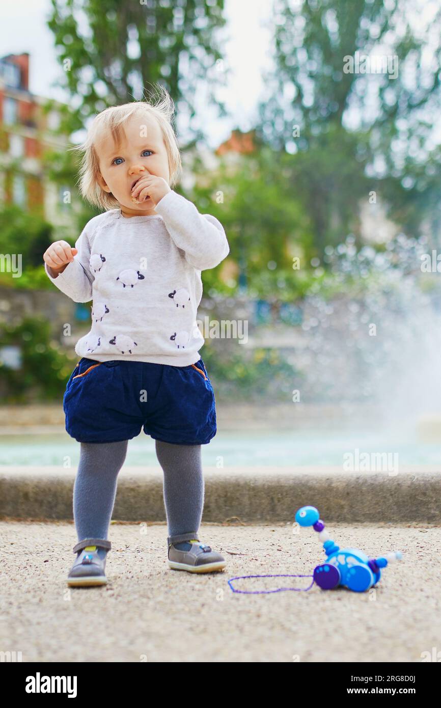 Adorabile bambina all'aperto che mangia pane nel parco. Bambino che gioca vicino alla fontana in una strada di Parigi. Attività all'aperto per bambini Foto Stock