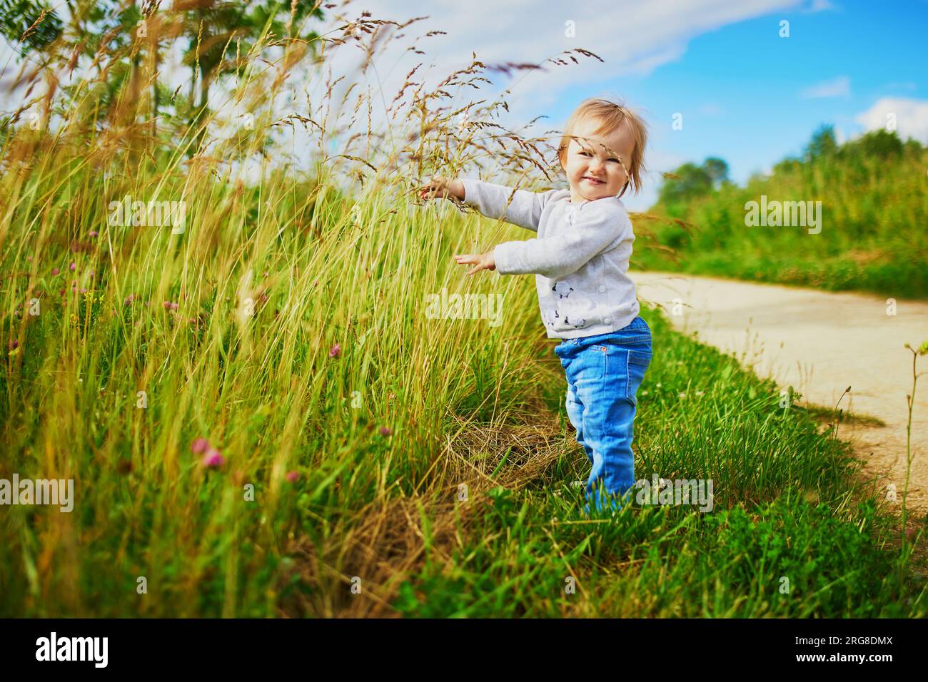 Adorabile bambina che cammina su un campo verde. Bambini piccoli che si divertono all'aperto. Ragazzo che esplora la natura Foto Stock