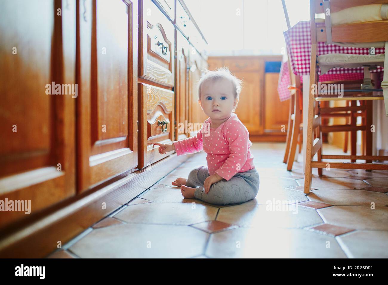 Bambina seduta sul pavimento in cucina. Bambino che strizza a casa ed esplora le cose intorno a lei Foto Stock