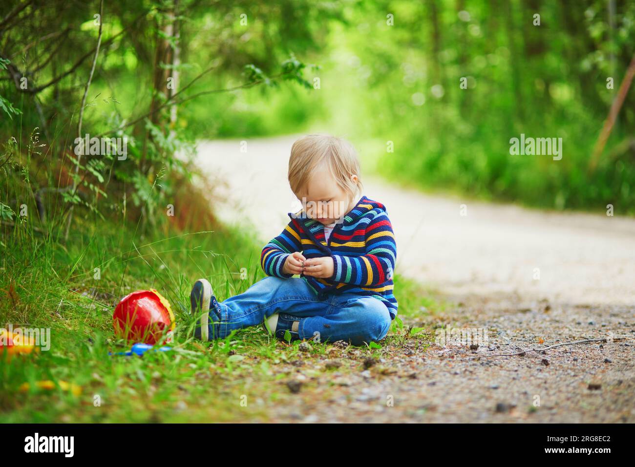 Adorabile bambina nella foresta, seduto a terra e giocando con pietre e coni di pino. Bambini piccoli che si divertono all'aperto. Ragazzo che esplora la natura Foto Stock