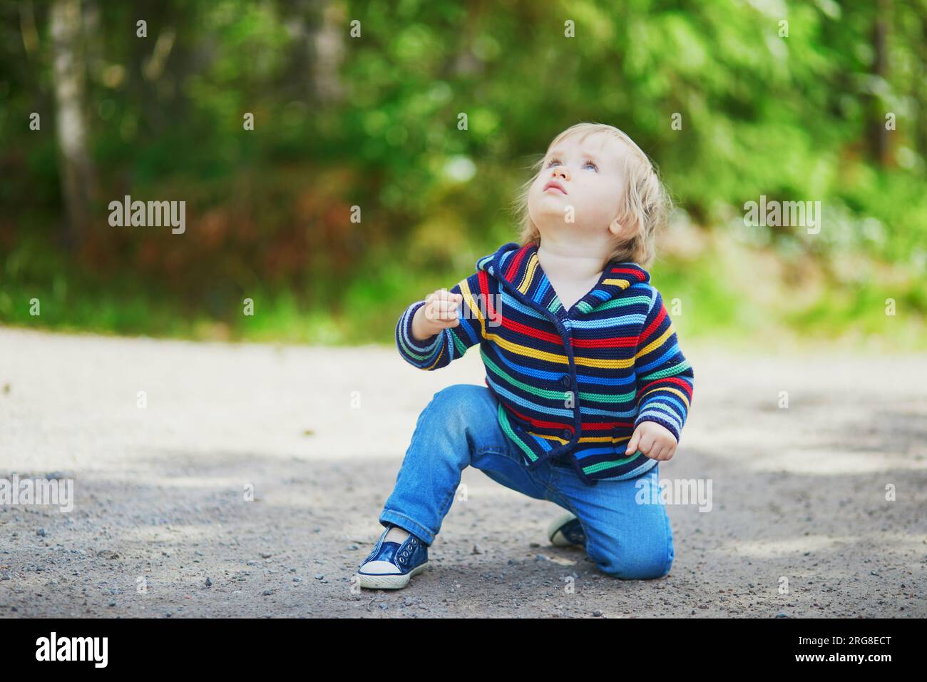 Adorabile bambina nella foresta, seduta per terra e guardando il cielo. Bambini piccoli che si divertono all'aperto. Ragazzo che esplora la natura Foto Stock