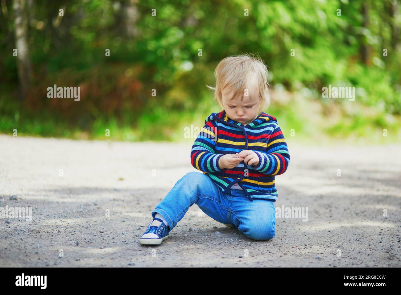 Adorabile bambina nella foresta, seduta per terra e giocando con le pietre. Bambini piccoli che si divertono all'aperto. Ragazzo che esplora la natura Foto Stock