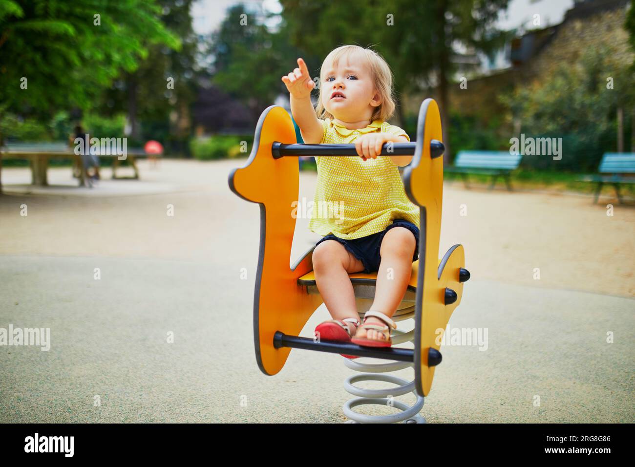 Adorabile bimba che si diverte con il ciclista primaverile nel parco giochi. Attività all'aperto per bambini Foto Stock