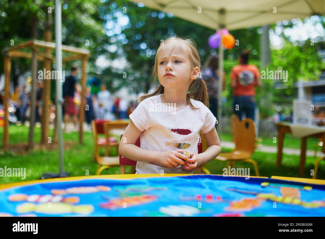 Adorabile bambina in età prescolare che gioca a un gioco da tavolo all'aperto. Bambino infelice che non ama perdere Foto Stock