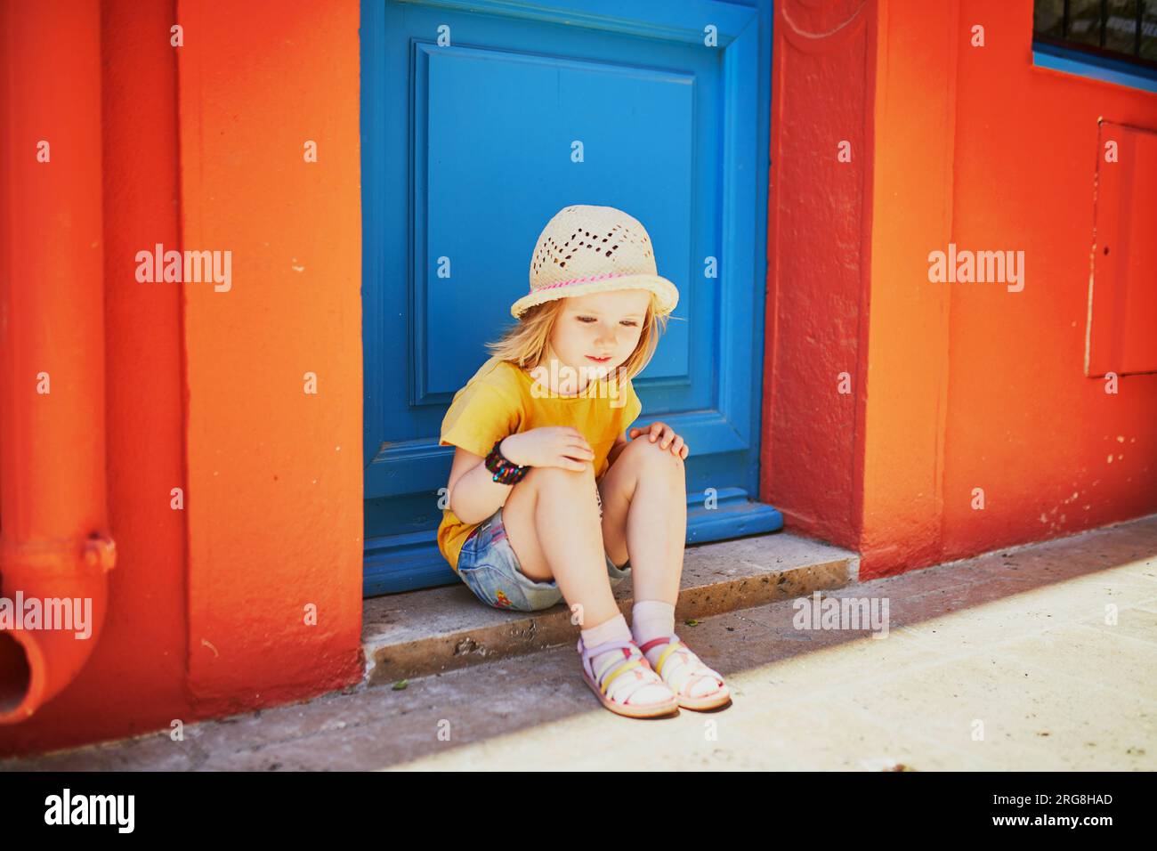 Adorabile bambina di tre anni seduta in una strada della bellissima città mediterranea di Collioure in Francia. Viaggiare con i bambini. Vacanze con bambini Foto Stock