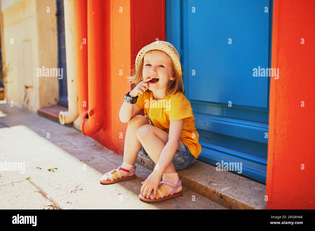 Adorabile bambina di tre anni seduta in una strada della bellissima città mediterranea di Collioure in Francia. Viaggiare con i bambini. Vacanze con bambini Foto Stock