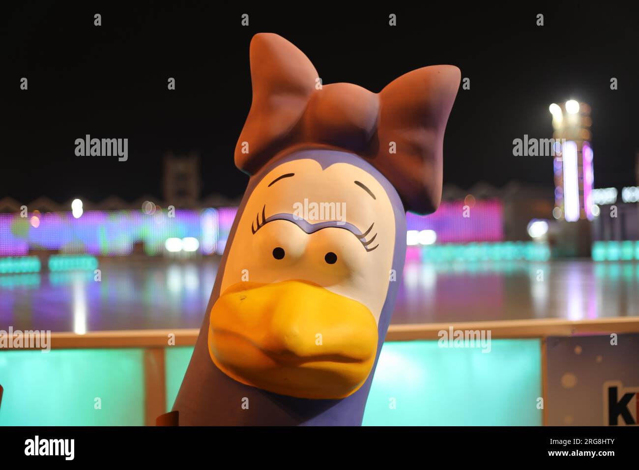 Volto espressivo della bambola uccellino con un fiocco sulla testa; esterno, sfondo sfocato della pista di pattinaggio illuminata al buio; concetto di emozione ed espressione Foto Stock