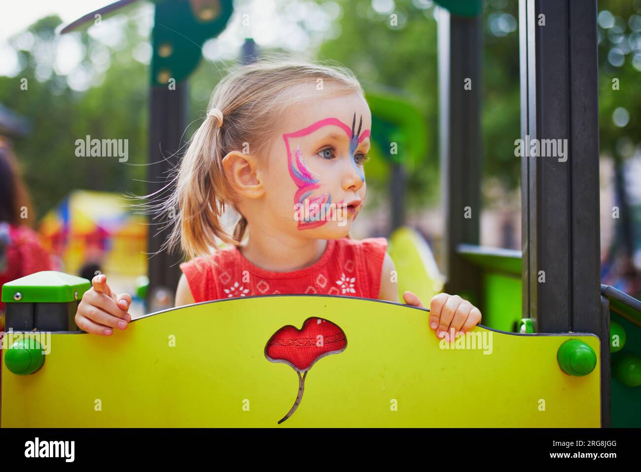 Bambina prescolastica che dipinge il viso a farfalla all'aperto. I bambini dipingono il viso. Attività creative per bambini Foto Stock