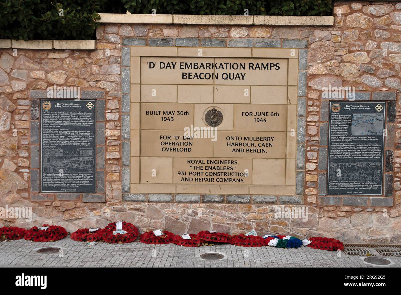 Un D-Day Memorial presso le rampe di imbarco di Beacon Quay a Torquay, Devon. Una fila di ghirlande di papavero è stata posata davanti al monumento. Foto Stock