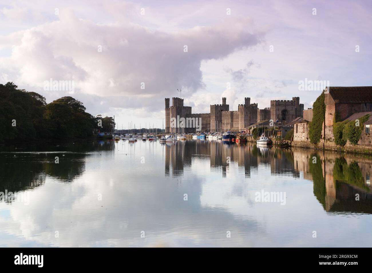 Una vista suggestiva del castello di Caernarfon (Caernarvon) nel Gwynedd, nel Galles del Nord, con numerose barche sull'acqua. Il castello fu costruito dal re inglese Edoardo i intorno al 1283, sul sito di una fortezza romana e Norman motte. Foto Stock