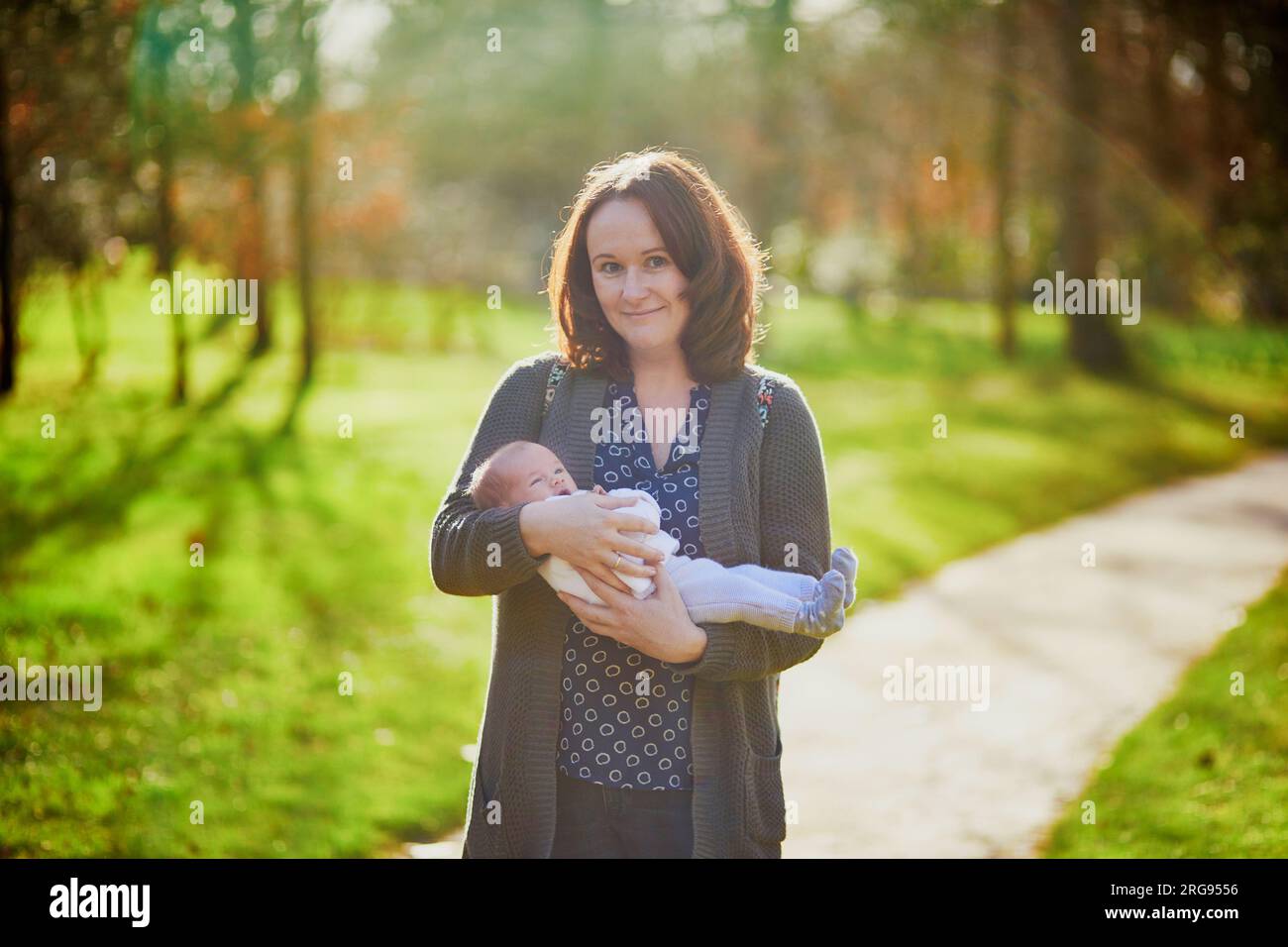 Madre che tiene tra le braccia una bambina di 4 settimane. un bambino di un mese in mano alla mamma all'aperto. Prima passeggiata per un neonato Foto Stock