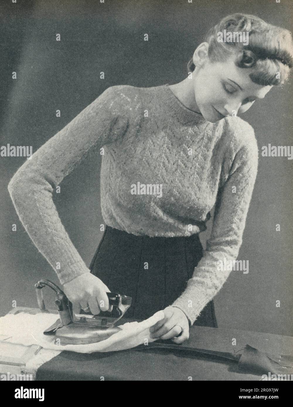 Donna che usa un ferro da stiro caldo per premere una cucitura sotto un panno umido. Foto Stock