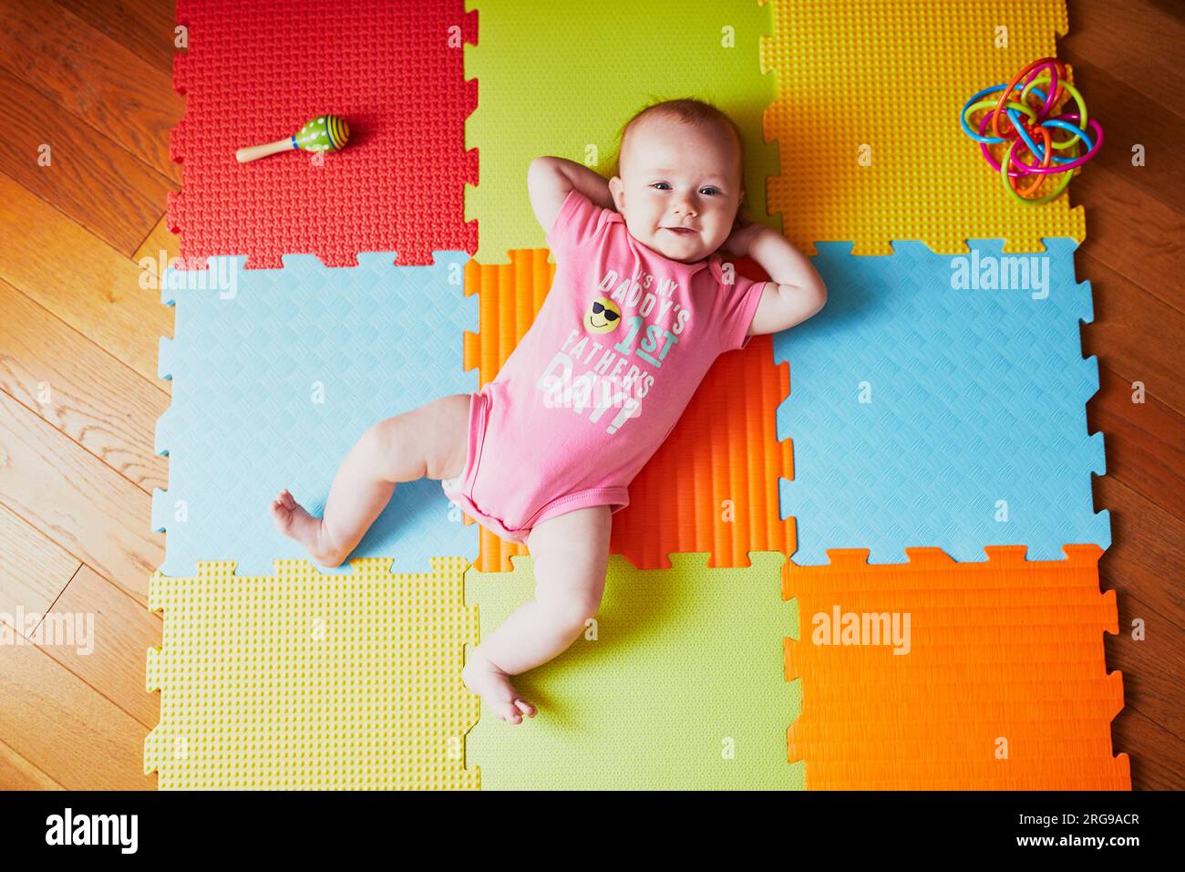 Bambina di 4 mesi sdraiata sul tappeto colorato sul pavimento con la scritta "è la giornata del primo padre di mio padre". Tappeto per attività per bambini Foto Stock