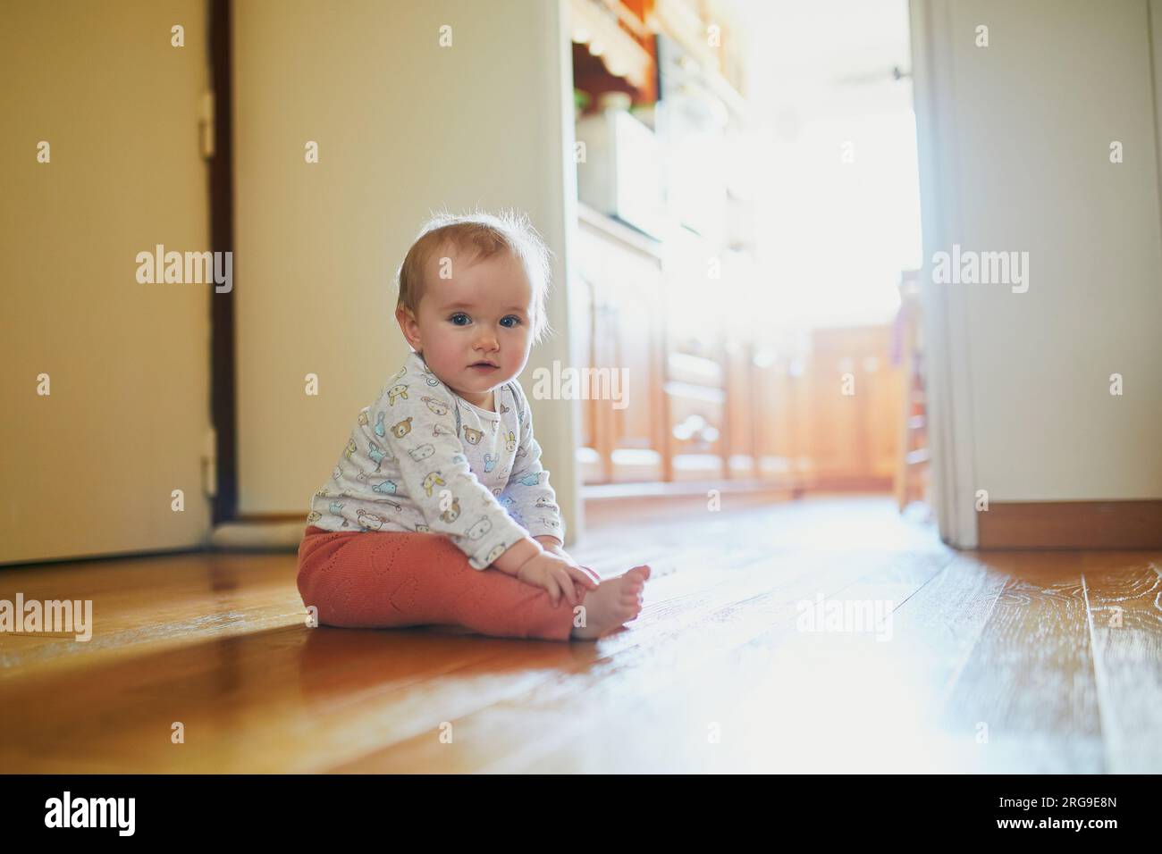 Bambina seduta sul pavimento a casa. Il bambino gattonava a casa ed esplorava la camera Foto Stock