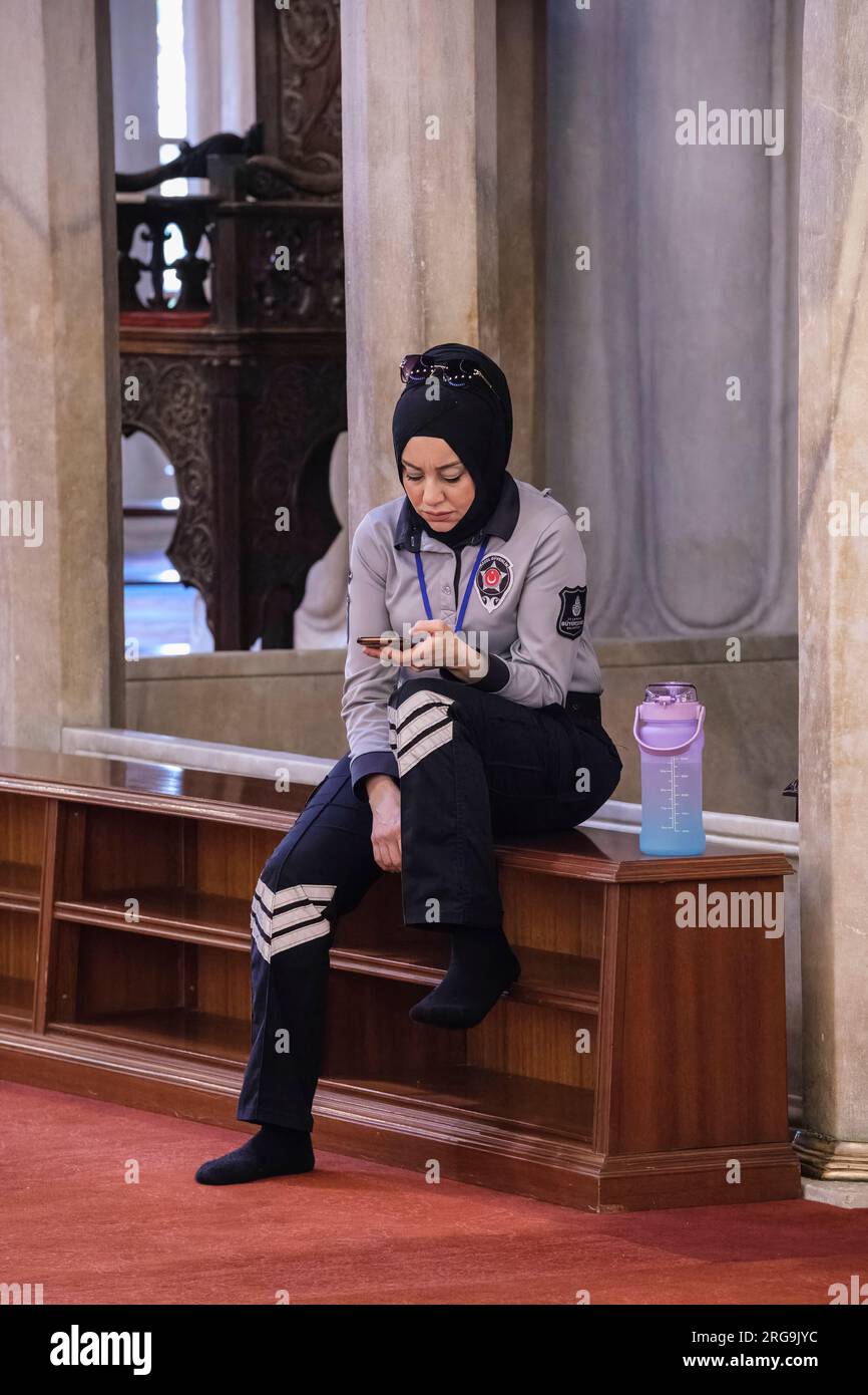 Istanbul, Turchia, Türkiye. Guardia di sicurezza che indossa un Hijab che controlla il suo telefono all'interno della Moschea Blu (Moschea del Sultano Ahmed) Foto Stock