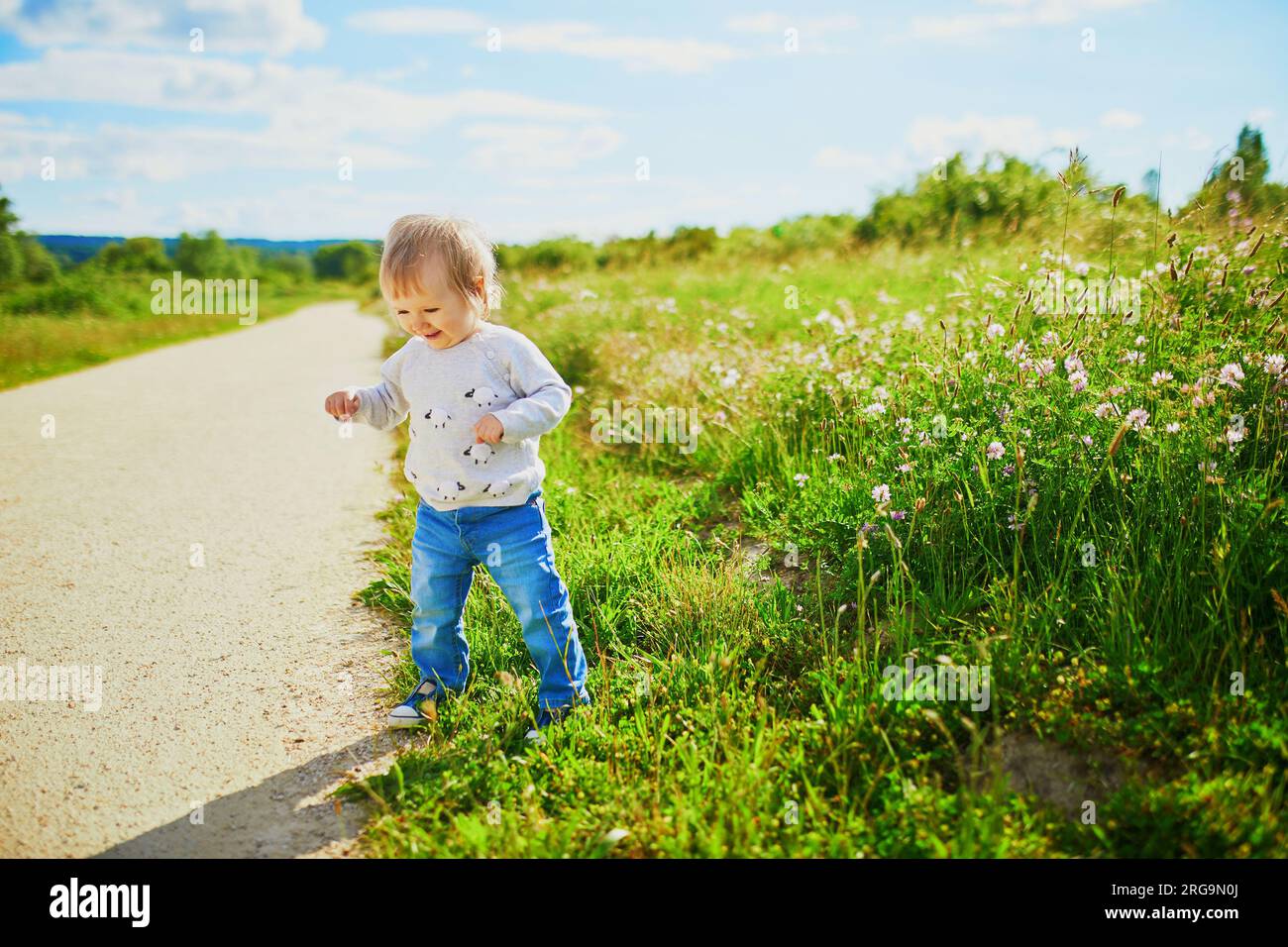 Adorabile bambina che cammina su un campo verde. Bambini piccoli che si divertono all'aperto. Ragazzo che esplora la natura Foto Stock