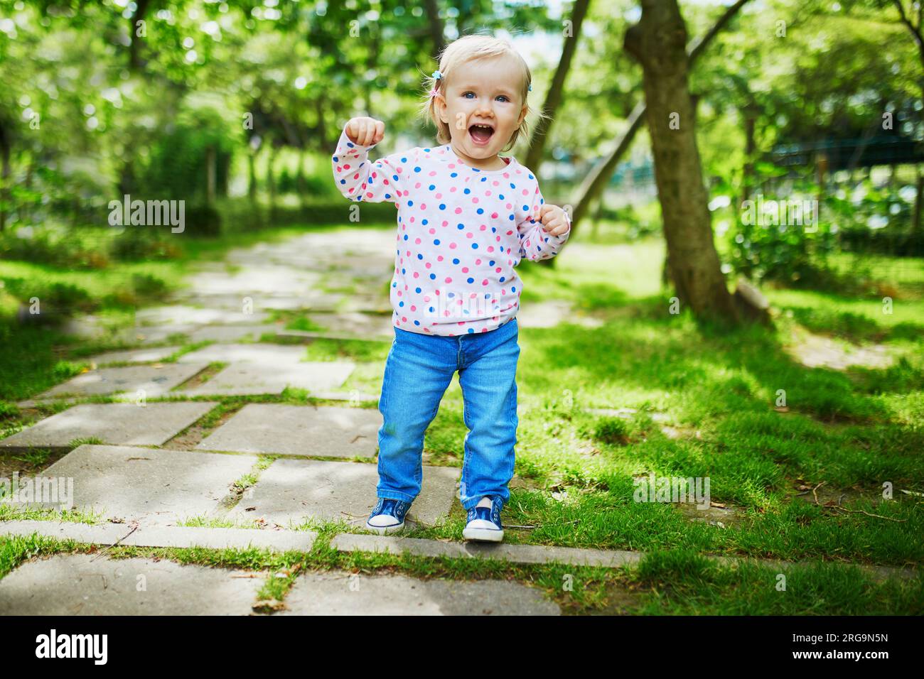 Adorabile bimba che cammina nel parco verde in un giorno d'estate. Bambini piccoli che si divertono all'aperto. Ragazzo che esplora la natura Foto Stock