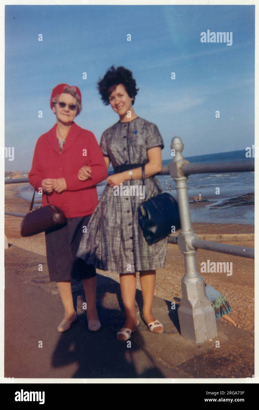 Una giovane donna e sua nonna che fanno una passeggiata lungo il lungomare della costa meridionale britannica - entrambi hanno belle borse ed entrambi sembrano leggermente spazzati dal vento! Settembre, 1962 Foto Stock