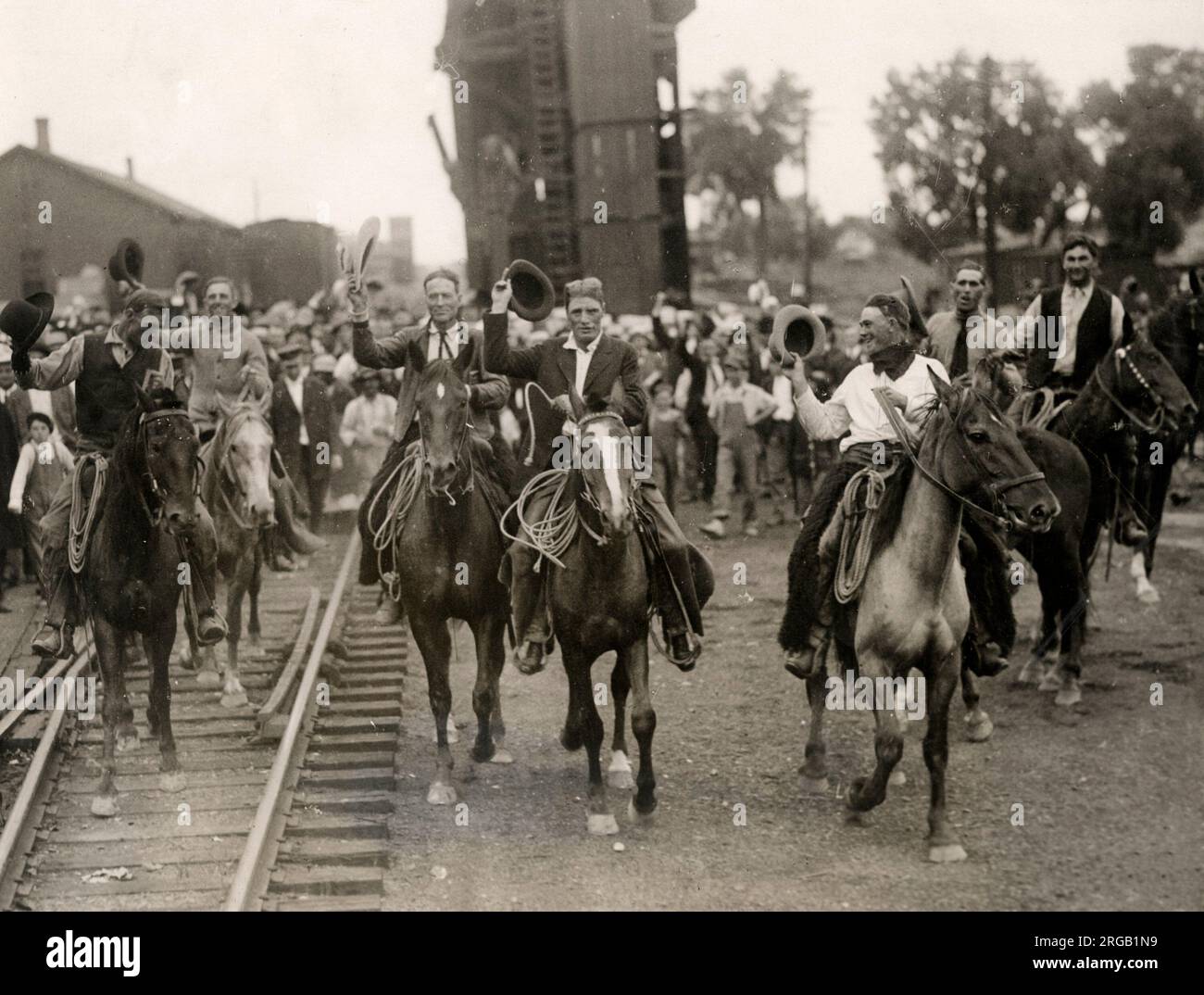 Nei primi anni del XX secolo vintage premere fotografia - rasserenante cowboy corsa lungo il binario ferroviario su cavalli, STATI UNITI D'AMERICA circa 1920s. Miglia città montana Foto Stock