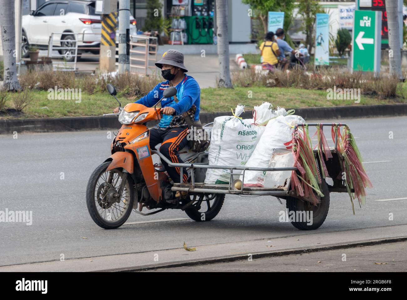 RATCHABURI, THAILANDIA, 18 ottobre 2022, Un uomo guida una moto con un sidecar carico di sacchi Foto Stock