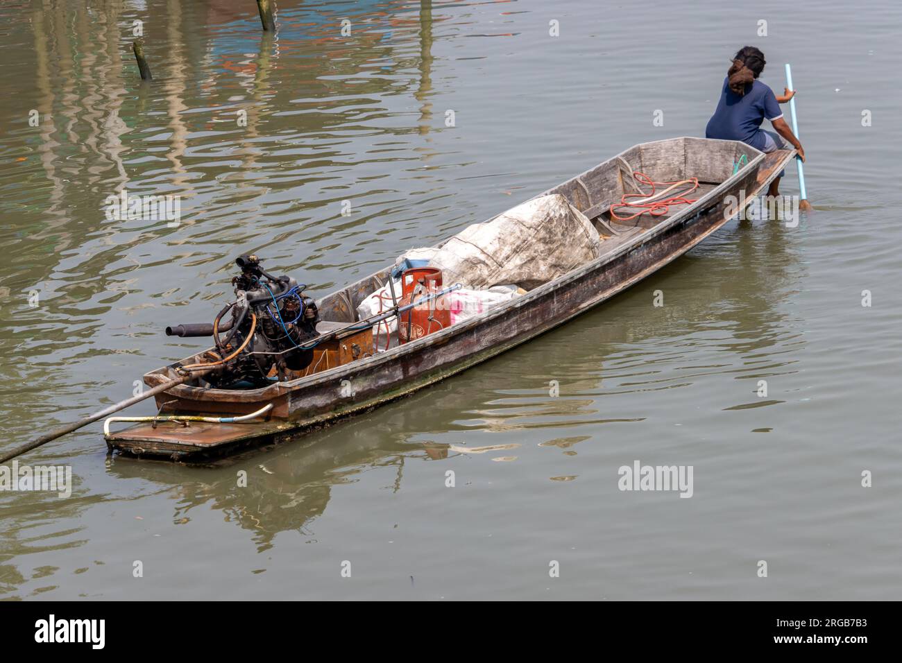 Una donna siede sulla prua di una barca e sta pagaiando con una pagaia, Thailandia Foto Stock