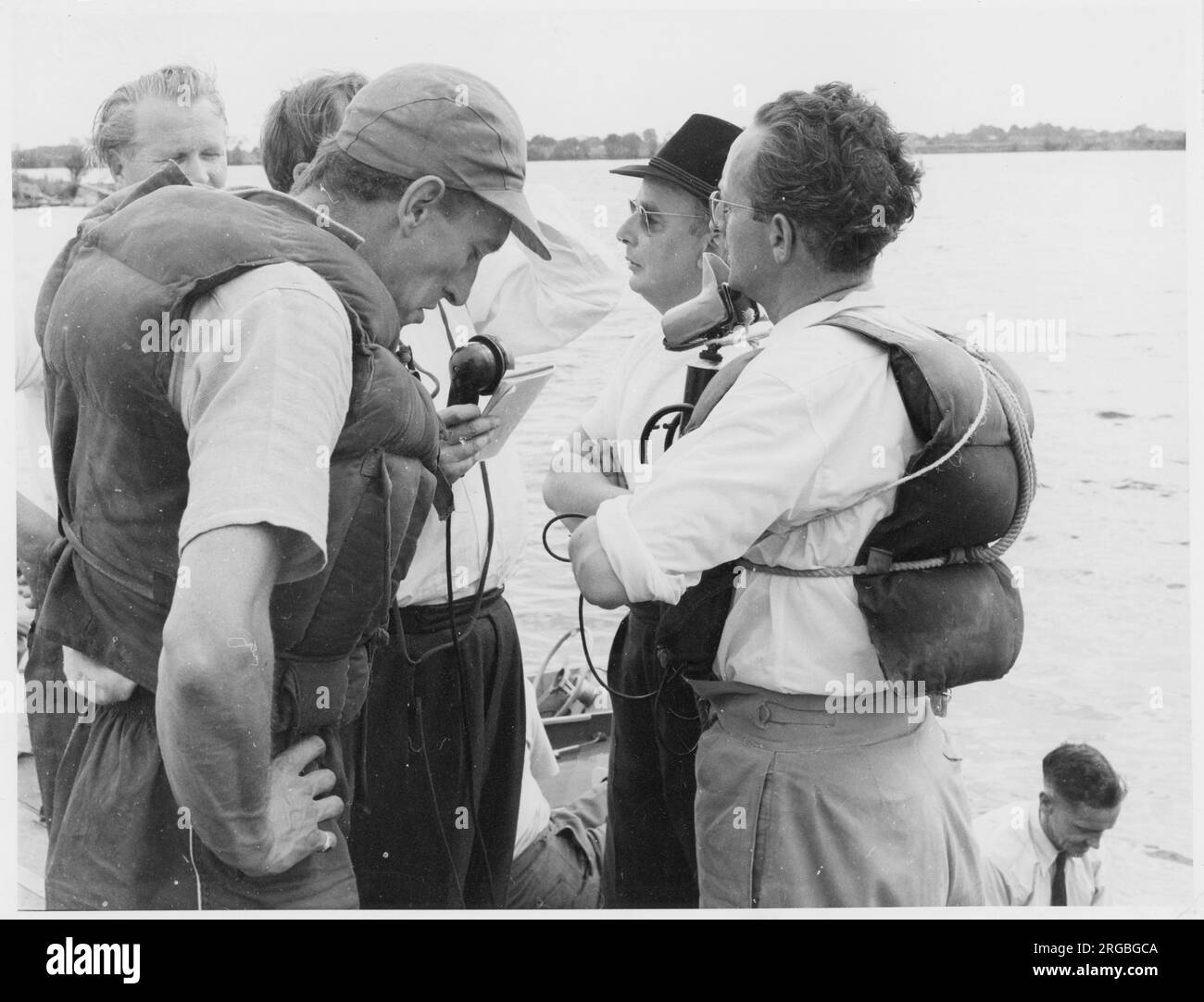 Raymond Baxter in giubbotto salvagente e berretto da palla base, durante le riprese sul luogo a bordo di una barca. Foto Stock Raymond Baxter in giubbotto salvagente e berretto da palla base, durante le riprese sul luogo a bordo di una barca. Foto Stock