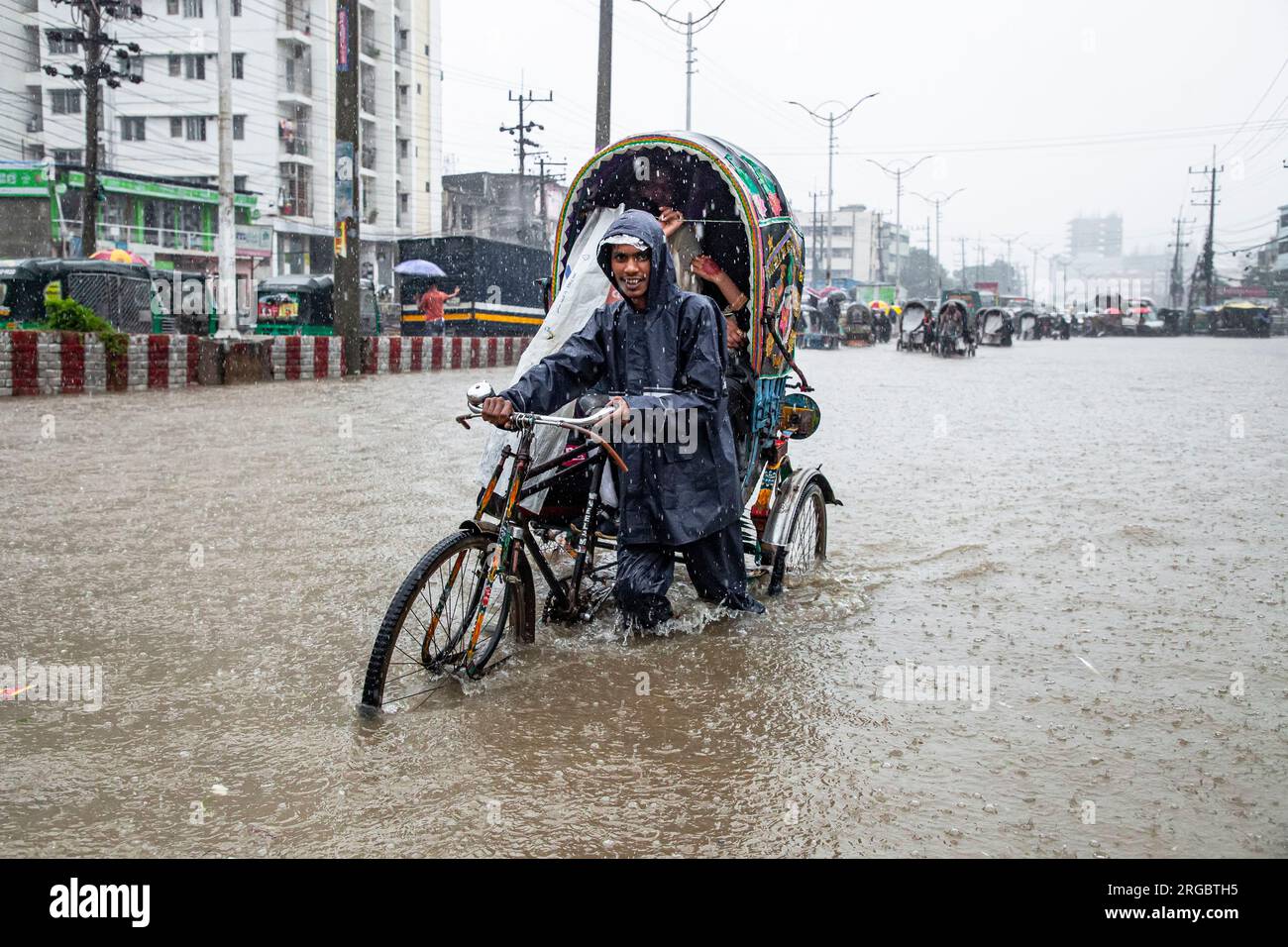 Risciò, furgoni, auto e biciclette attraversano le acque profonde della vita a Bordharhat a Chittagong. Ore di pioggia incessante hanno portato alla disboscamento delle acque in molte aree della città, causando sofferenze indescrivibili alle persone. Chittagong, Bangladesh. Foto Stock