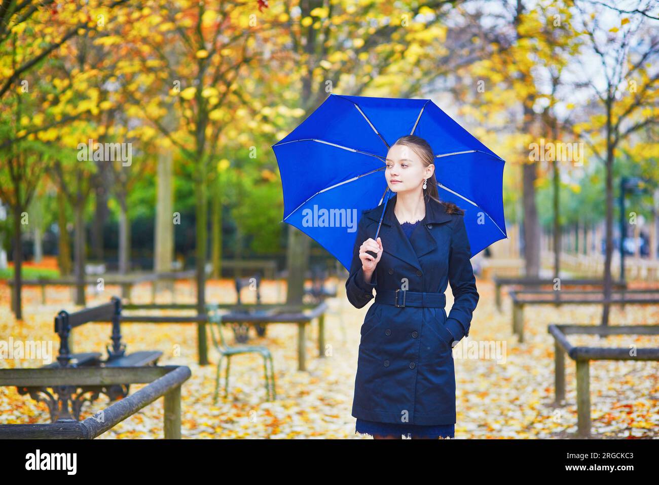 Bellissima giovane donna con ombrello blu nel giardino lussemburghese di Parigi in un giorno di pioggia primaverile o autunnale Foto Stock