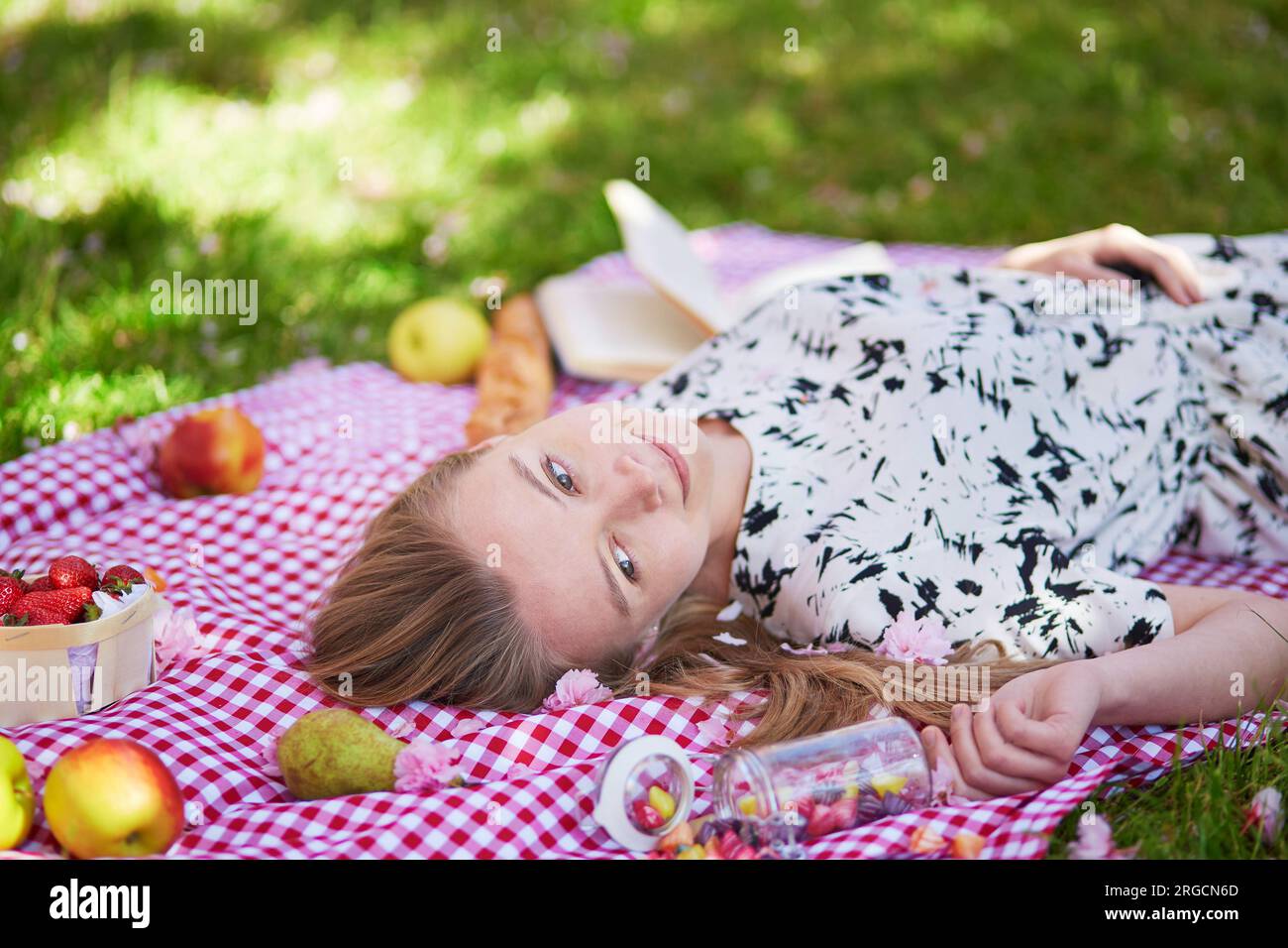 Bella giovane donna che fa un picnic a parc, sdraiata sulla schiena con dei frutti intorno a lei Foto Stock