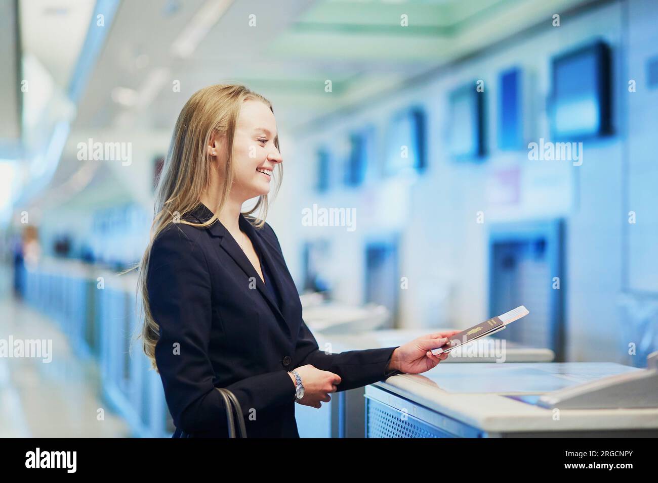 Giovane donna d'affari all'aeroporto internazionale al banco del check-in, che consegna il passaporto a un ufficiale e aspetta la sua carta d'imbarco Foto Stock