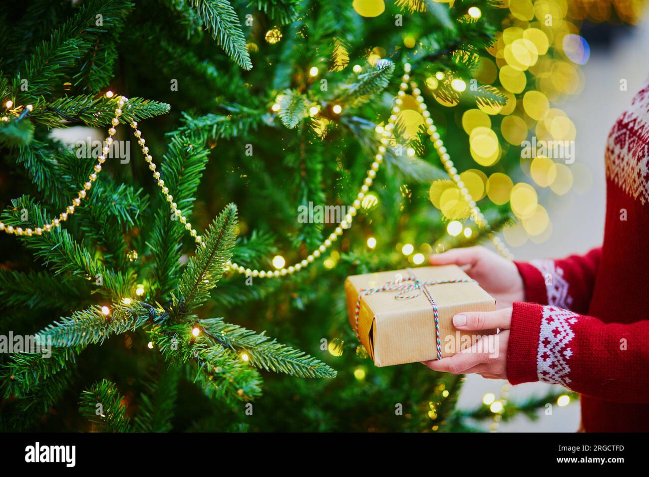 Mani di una donna che tiene un regalo di Natale vicino all'albero di Capodanno decorato con luci e perline Foto Stock