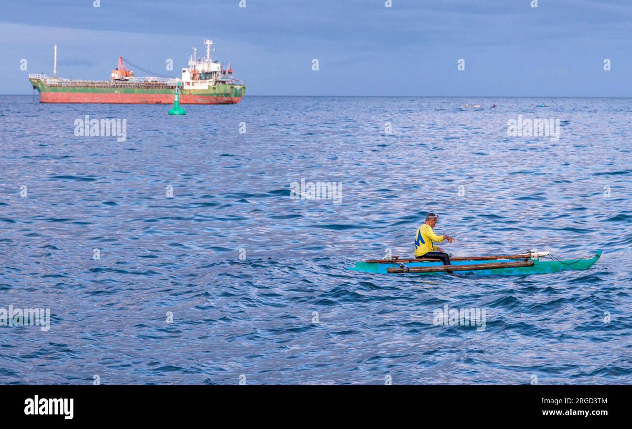 Dumaguete, Isola di Negros, Filippine-01 febbraio 2023: Al crepuscolo, l'uomo lancia reti e si tuffa in acqua per pescare e una grande nave è ancorata vicino Foto Stock
