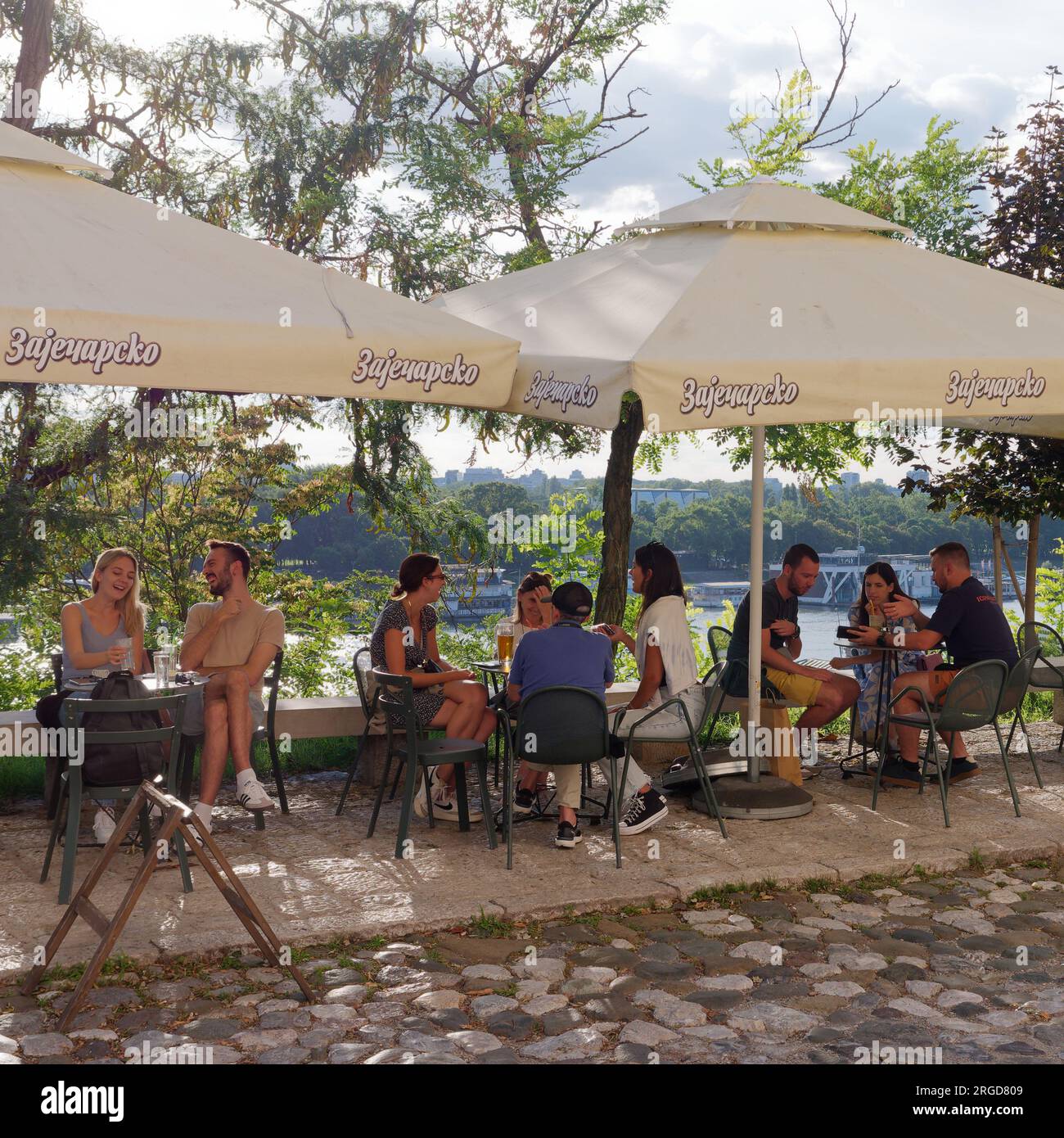I clienti di un caffè/ristorante in una strada acciottolata in una giornata estiva con vista sul fiume Sava nella città di Belgrado, Serbia. Agosto 8,2023. Foto Stock
